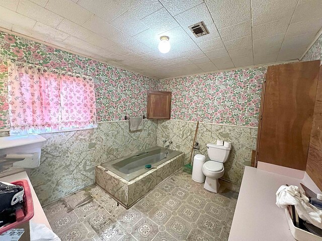 207 Elm St, Silsbee, TX 77656 - full bathroom featuring wallpapered walls, wainscoting, toilet, a bath, and tile walls