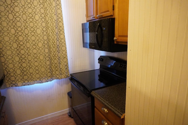 kitchen with black appliances, dark stone countertops, and hardwood / wood-style flooring