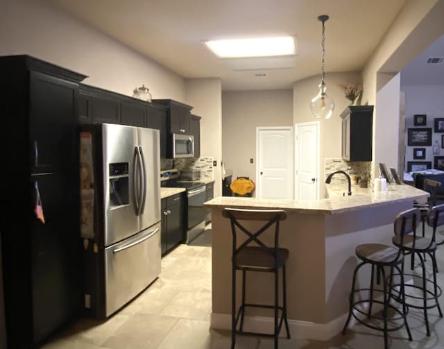 kitchen with stainless steel appliances, dark cabinetry, a breakfast bar area, and tasteful backsplash