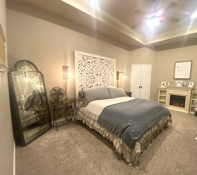 bedroom with a ceiling fan, a lit fireplace, a tray ceiling, carpet flooring, and a closet