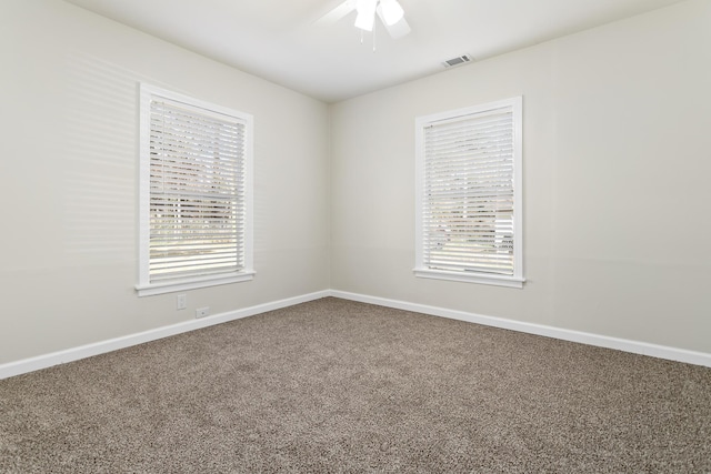 carpeted empty room with baseboards, a wealth of natural light, a ceiling fan, and visible vents