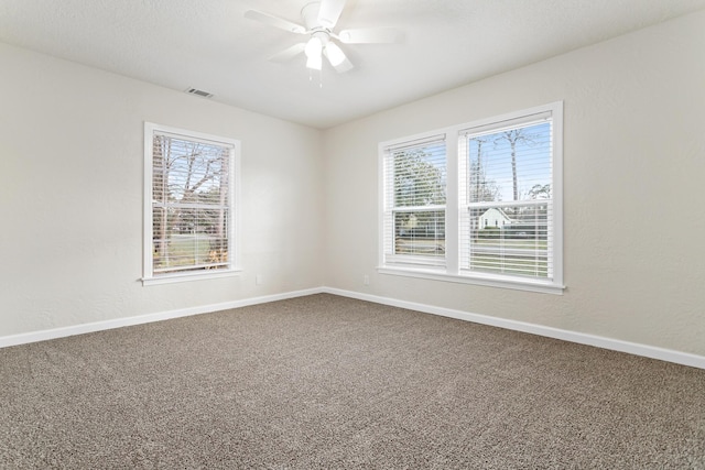 carpeted spare room featuring a healthy amount of sunlight, baseboards, ceiling fan, and visible vents
