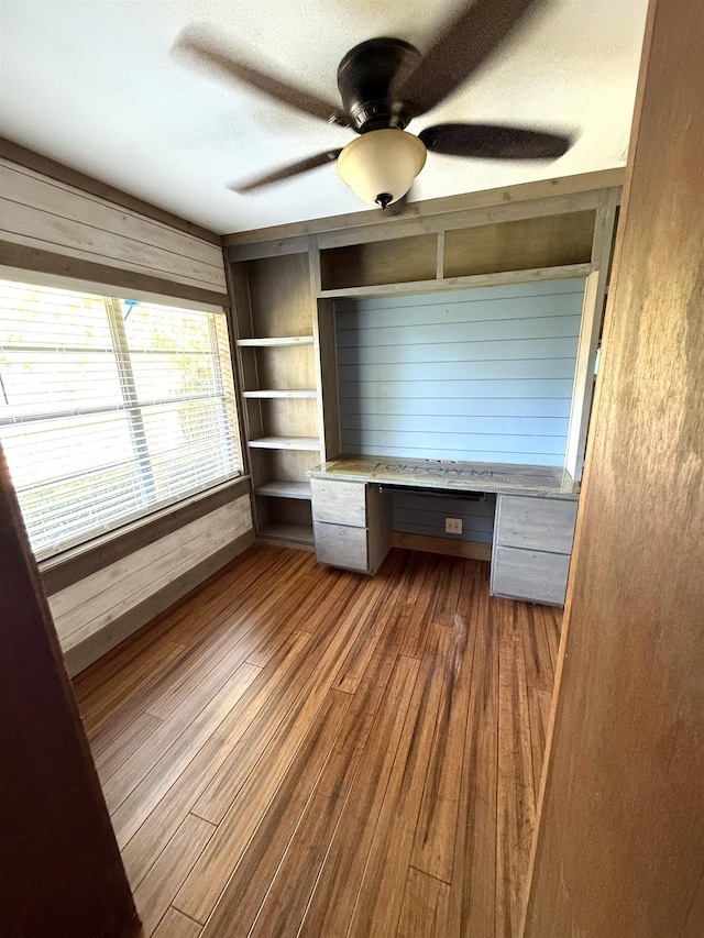 interior space with ceiling fan, built in desk, a textured ceiling, wood-type flooring, and a closet