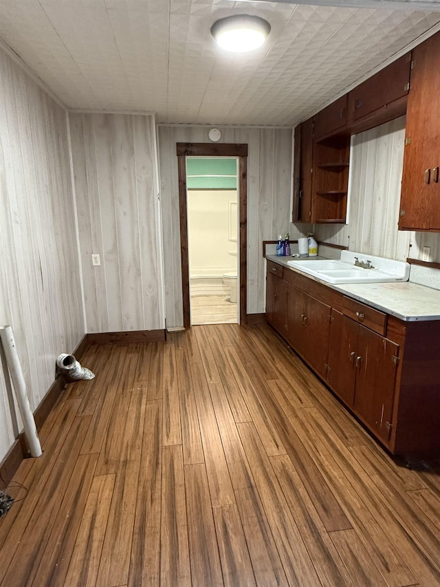 kitchen with dark brown cabinets, wood walls, light wood-type flooring, and sink