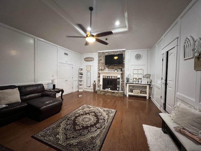 living room with dark wood-type flooring, crown molding, a brick fireplace, ceiling fan, and a tray ceiling