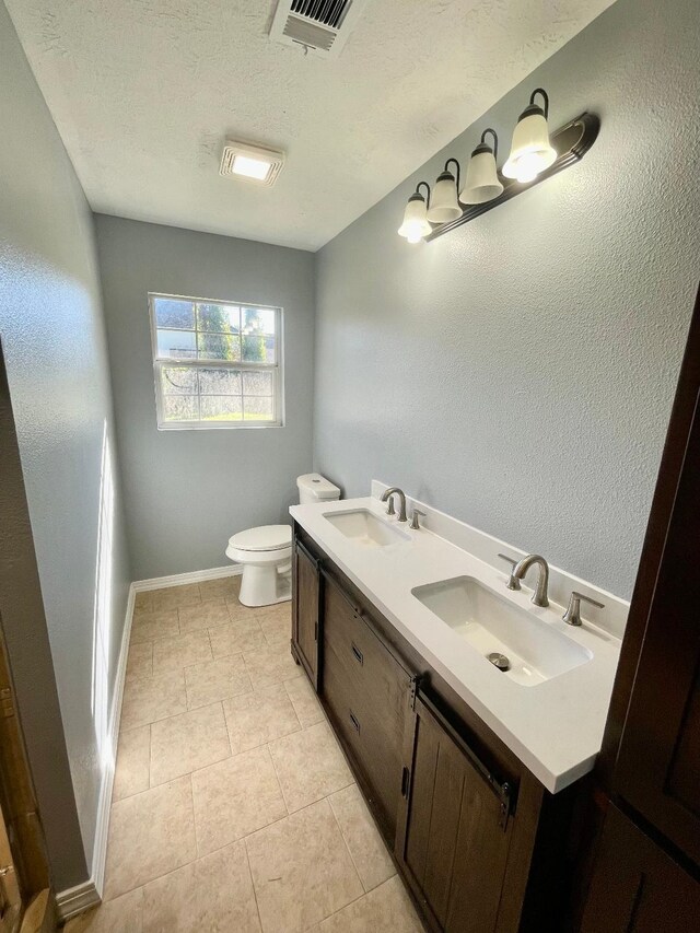 bathroom with tile patterned flooring, a textured ceiling, vanity, and toilet