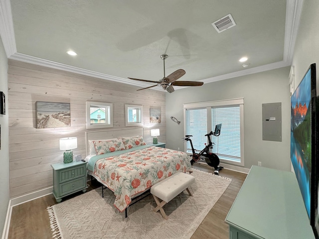 bedroom with ornamental molding, ceiling fan, wooden walls, wood-type flooring, and electric panel