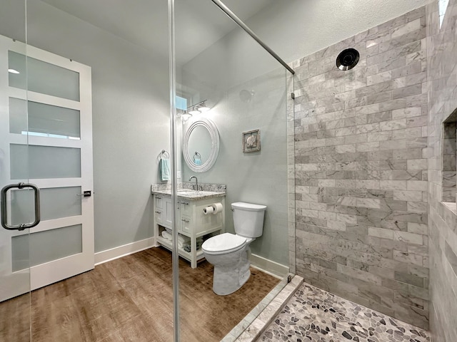 bathroom with hardwood / wood-style flooring, vanity, toilet, and a tile shower