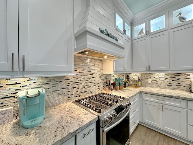 kitchen featuring custom exhaust hood, backsplash, white cabinets, light stone countertops, and stainless steel range with gas stovetop