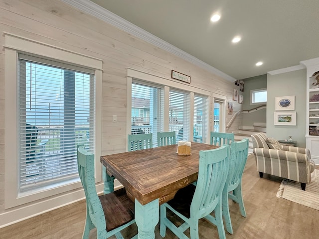 dining space with a wealth of natural light, wooden walls, light hardwood / wood-style floors, and ornamental molding