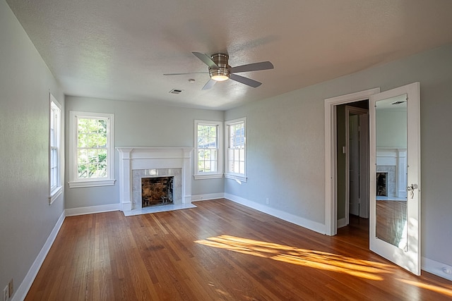 unfurnished living room with a tile fireplace, wood-type flooring, a textured ceiling, and ceiling fan