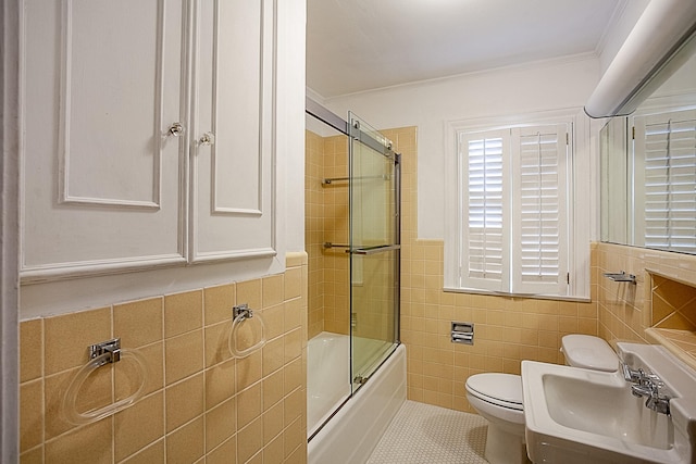 full bathroom with ornamental molding, sink, shower / bath combination with glass door, tile walls, and toilet