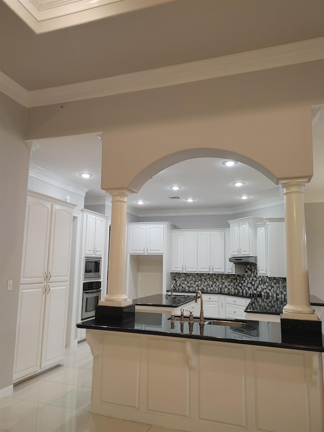 kitchen featuring backsplash, stainless steel appliances, decorative columns, white cabinets, and light tile patterned flooring