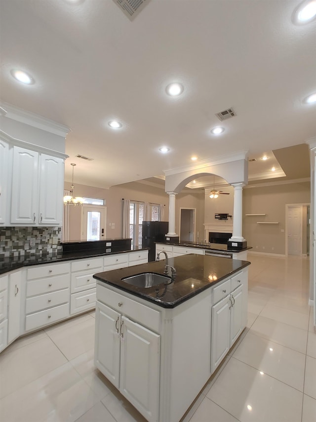 kitchen with sink, decorative columns, a kitchen island with sink, decorative backsplash, and white cabinets