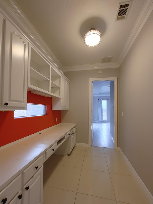 kitchen with ornamental molding, built in desk, white cabinets, and light tile patterned floors