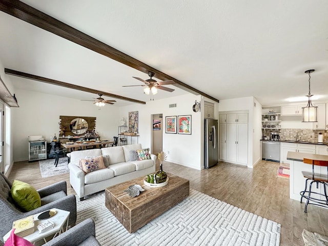 living room with light wood-style flooring, visible vents, baseboards, and beam ceiling