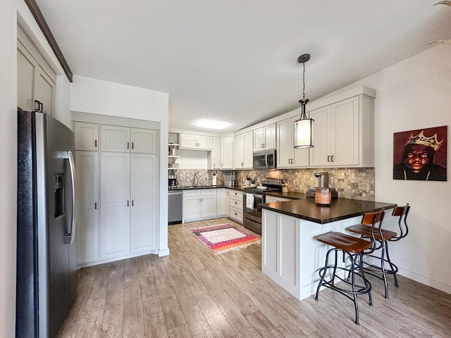 kitchen featuring light wood finished floors, tasteful backsplash, dark countertops, appliances with stainless steel finishes, and a peninsula