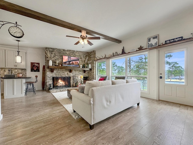 living area featuring light wood-style flooring, a fireplace, ceiling fan, and beamed ceiling