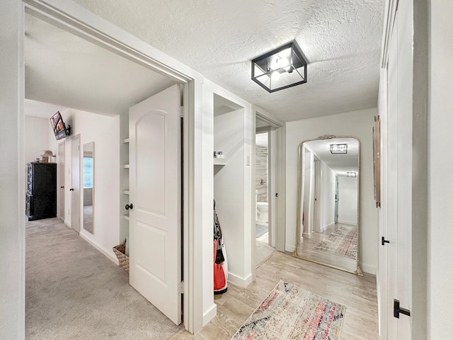 corridor with a textured ceiling and light wood finished floors