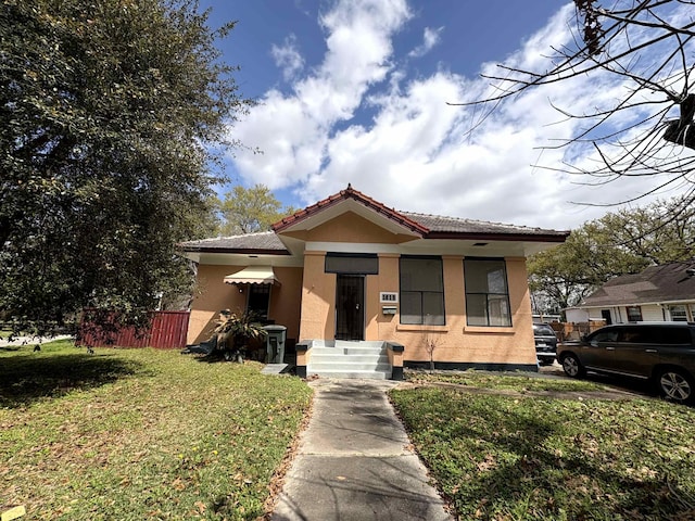 bungalow-style home with stucco siding, a tile roof, and a front yard