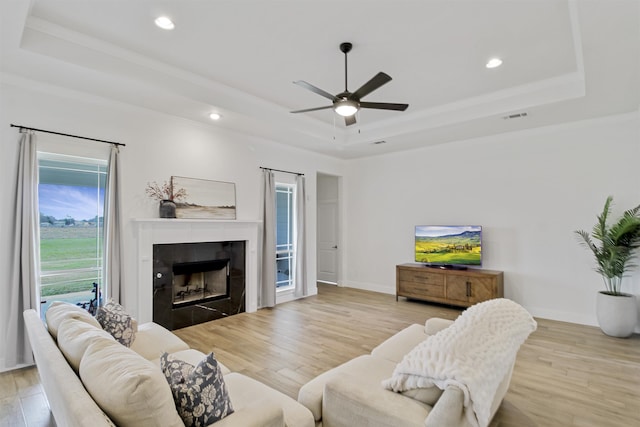 living room with a tray ceiling, wood finished floors, visible vents, and a ceiling fan