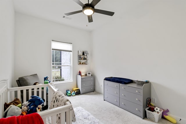 carpeted bedroom featuring visible vents, a ceiling fan, and a crib