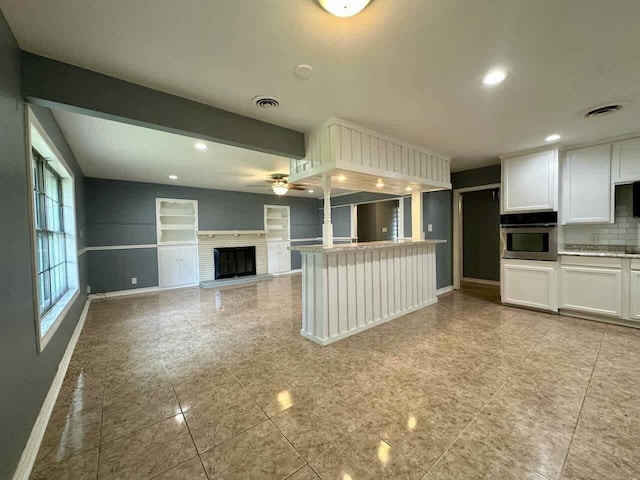 kitchen featuring backsplash, white cabinets, oven, ceiling fan, and kitchen peninsula