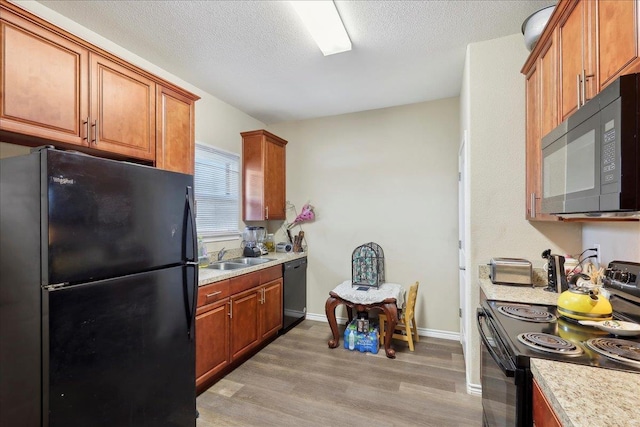 kitchen with light wood finished floors, brown cabinetry, light countertops, a textured ceiling, and black appliances