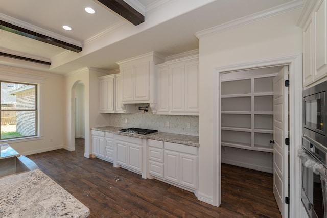 kitchen with arched walkways, stainless steel appliances, white cabinetry, ornamental molding, and dark wood-style floors