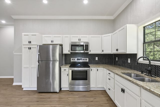 kitchen featuring crown molding, appliances with stainless steel finishes, white cabinetry, a sink, and light stone countertops