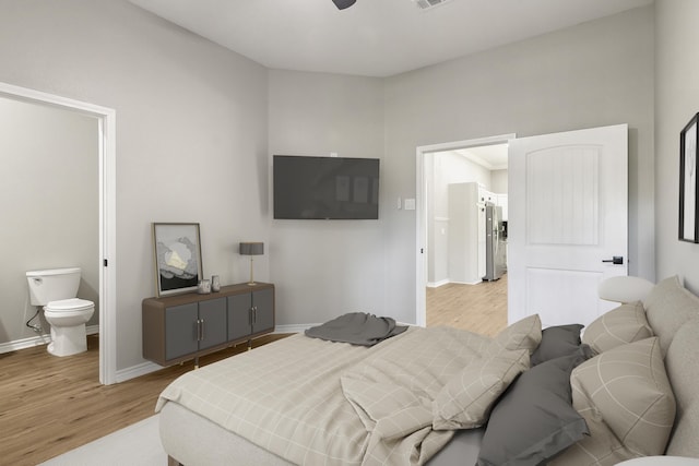 bedroom featuring visible vents, baseboards, light wood-type flooring, freestanding refrigerator, and ensuite bath