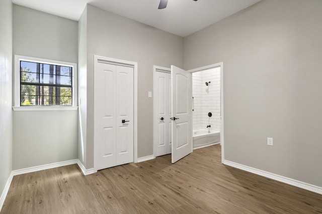 unfurnished bedroom featuring multiple closets, ensuite bathroom, ceiling fan, wood finished floors, and baseboards