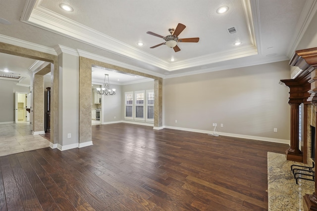 unfurnished living room featuring ceiling fan with notable chandelier, a fireplace with flush hearth, visible vents, a tray ceiling, and dark wood finished floors