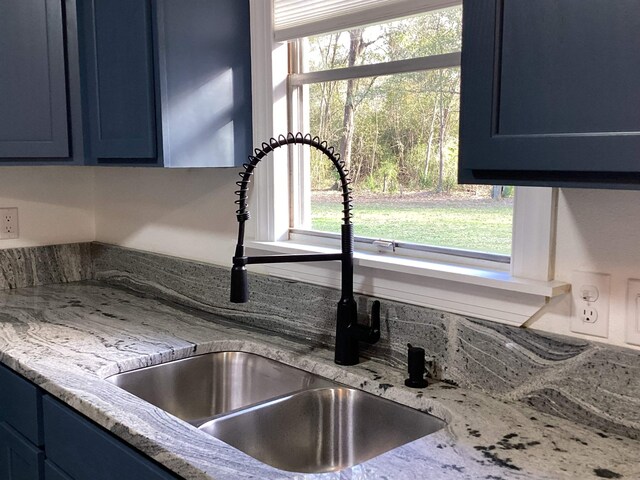 room details with blue cabinetry, sink, and light stone counters