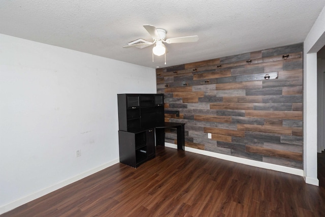 unfurnished office with a textured ceiling, dark hardwood / wood-style floors, ceiling fan, and wood walls