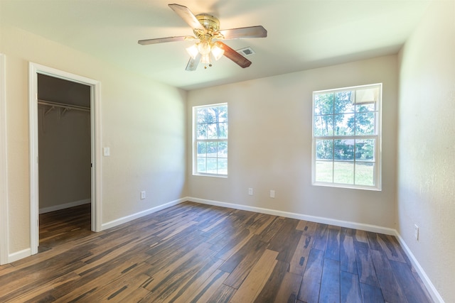 unfurnished bedroom featuring ceiling fan, a spacious closet, multiple windows, dark hardwood / wood-style flooring, and a closet