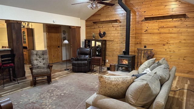 interior space featuring wooden walls, ceiling fan, a wood stove, a textured ceiling, and vaulted ceiling