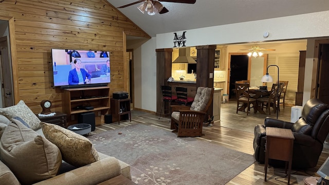 living room featuring hardwood / wood-style flooring, ceiling fan, vaulted ceiling, and wood walls