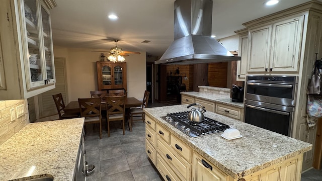 kitchen featuring island exhaust hood, ceiling fan, appliances with stainless steel finishes, light stone countertops, and a kitchen island