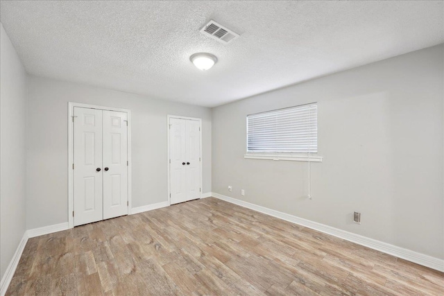 1663 Bluebonnet St, Vidor, TX 77662 - unfurnished bedroom with multiple closets, light wood-type flooring, a textured ceiling, and baseboards