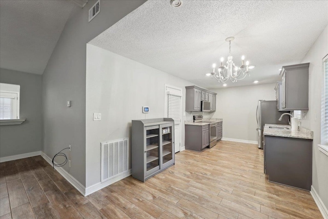 1663 Bluebonnet St, Vidor, TX 77662 - kitchen with appliances with stainless steel finishes, gray cabinetry, light wood-style floors, a chandelier, and baseboards