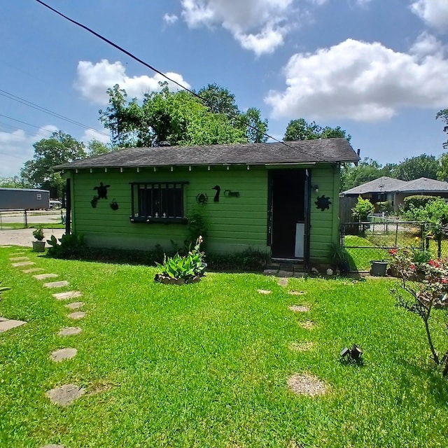 rear view of property featuring a lawn, a shingled roof, and fence