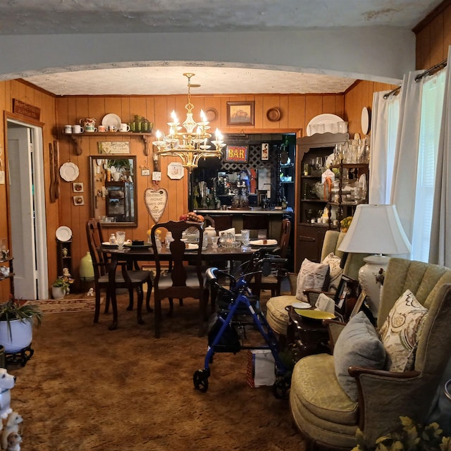 dining space featuring carpet, a notable chandelier, and wooden walls