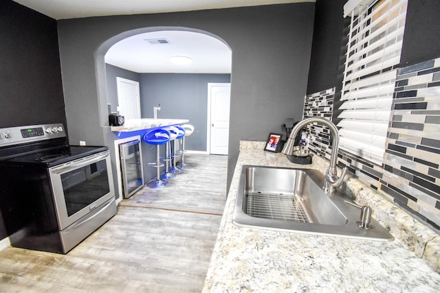 kitchen with stainless steel range with electric stovetop, sink, wine cooler, decorative backsplash, and light wood-type flooring