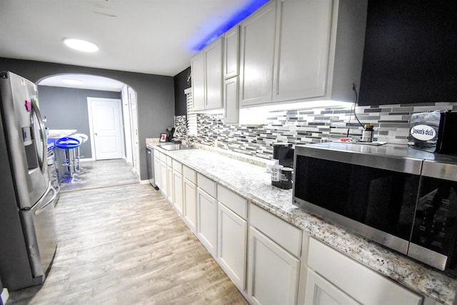 kitchen with appliances with stainless steel finishes, backsplash, sink, light hardwood / wood-style flooring, and white cabinetry