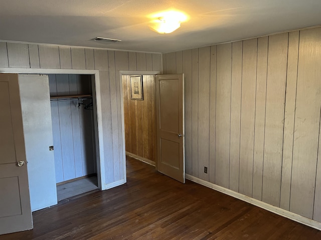 unfurnished bedroom featuring dark hardwood / wood-style floors, wooden walls, and a closet