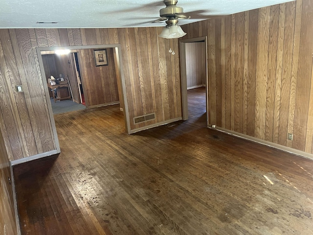 unfurnished room featuring a textured ceiling, dark hardwood / wood-style floors, ceiling fan, and wooden walls