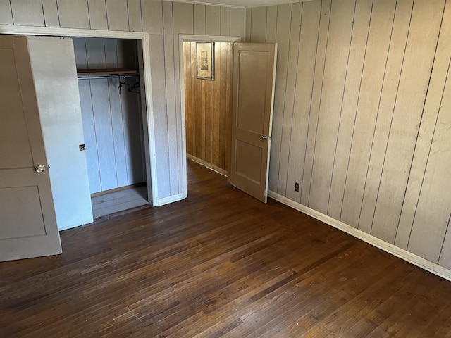 unfurnished bedroom with wood walls, dark hardwood / wood-style flooring, and a closet