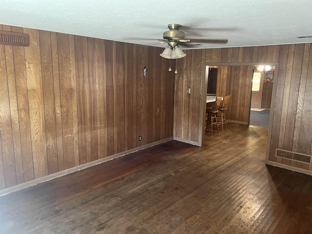 spare room with ceiling fan, wooden walls, dark wood-type flooring, and a textured ceiling