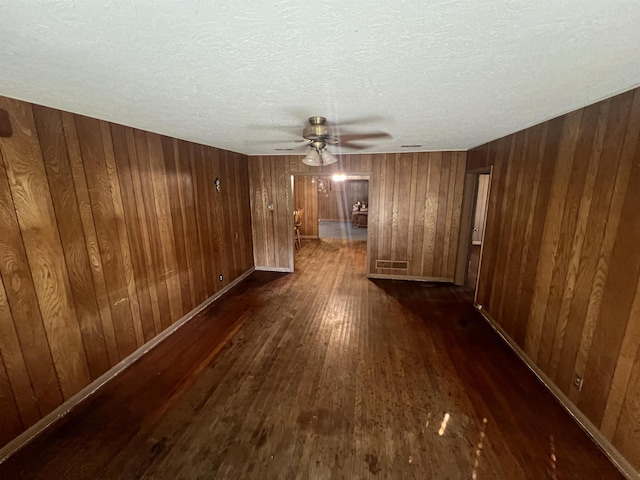 spare room featuring a textured ceiling, dark wood-type flooring, ceiling fan, and wooden walls